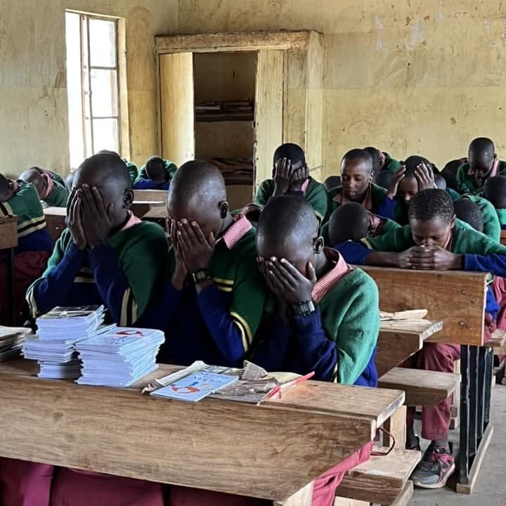 Schoolchildren praying at their desks in a village classroom